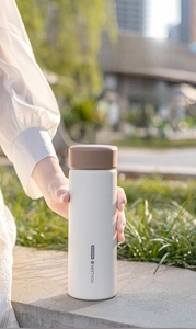 Detail of hand holding a frosted white stainless steel vacuum flask with a brown lid