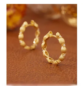 Macro detail of gold-brushed earrings with sparkling zircon on a leather background