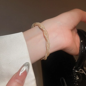 Close-up of golden woven mesh bracelet with twisted wave design on model's wrist