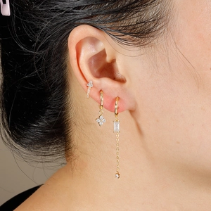 Golden earrings set with sparkling zircons and clover charms worn by model