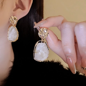 Detail showing irregular hammered gold earrings with creamy white marble resin drops
