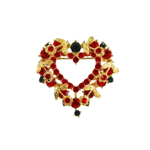 Detailed close-up of heart-shaped gold brooch with red crystals and rhinestone tassels