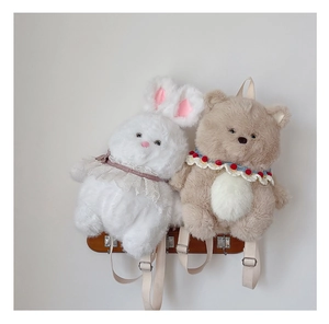 Detail of plush bear and rabbit backpacks hanging on wooden hooks against a white wall