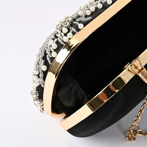 Close-up of black evening bag with faux pearls, silver beads and golden chain strap