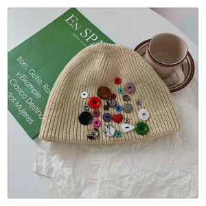 Detail of beige knit beanie with colorful buttons and green book on white background