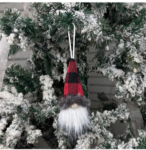 Close-up of a Christmas gnome ornament with red plaid hat hanging on a snowy tree branch