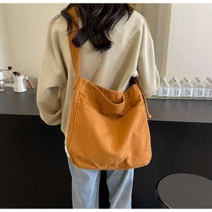 Detail of a brown canvas tote bag with front pocket and wide strap on a model