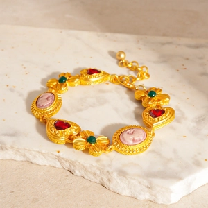 Detail of vintage gold bracelet with pink cameo portraits and red heart gems on marble