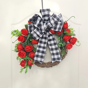 Handmade Christmas wreath with red roses and plaid bow on white door