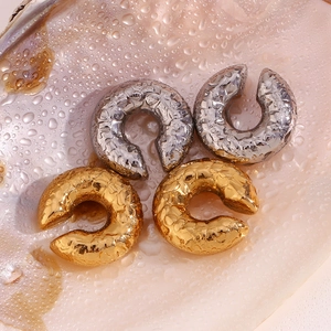 Macro detail of gold and silver chunky C-shaped earrings with hammered texture finish
