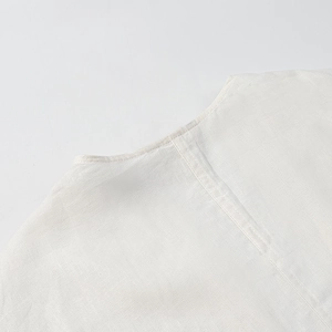 Close-up of white cotton linen fabric texture and neck stitching on loose batwing top
