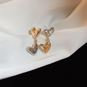 Detailed shot of two-tone gold and silver heart earrings on elegant white satin fabric