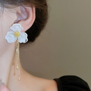 Detail of white acrylic flower earrings with long gold tassel chains on model