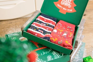 Two pairs of festive Christmas socks in a green holiday gift box on a wooden base