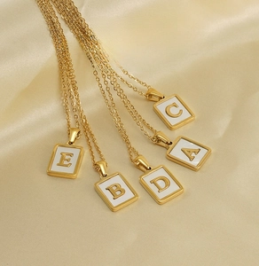 Macro shot of 26 initial shell necklaces in gold stainless steel on silk background