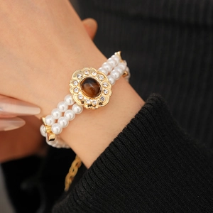 Dettaglio macro del bracciale di perle a doppio filo con chiusura a fiore dorato