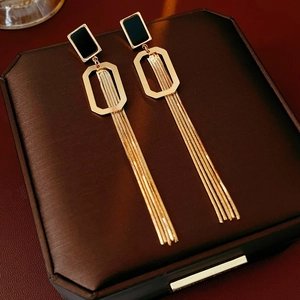 Détail de longues boucles d'oreilles à pompons dorés et carré noir sur boîte