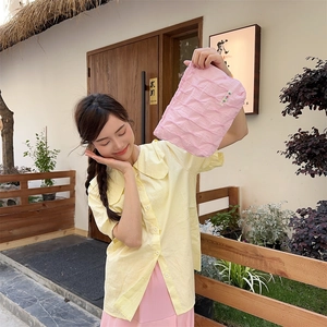 Detail showing pink quilted fabric clutch held by a model in a natural setting