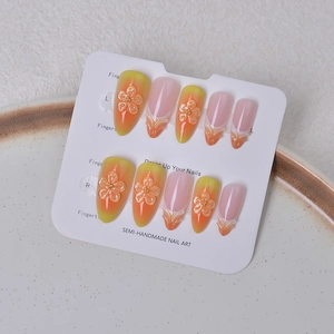 Detail of almond-shaped press-on nails with 3D floral accents and orange gradient design