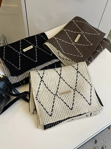 Detail of stacked handmade knitted scarves with diamond patterns in black, brown, and beige