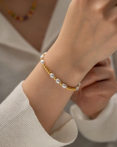 Nahaufnahme eines 18K vergoldeten Perlenarmbands mit weißen Perlen am Handgelenk