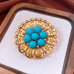Macro detail of vintage gold hollow flower brooch with blue turquoise and pink rhinestones
