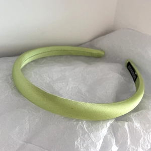Detail of light green satin headband with handmade label on white textured background