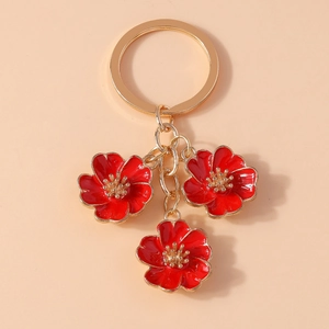 Detailed close-up of golden keychain with three red enamel cherry blossom flower charms