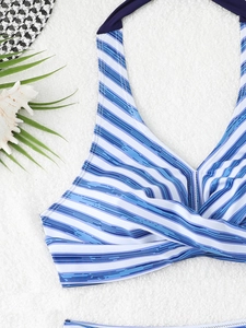 Dettaglio del top bikini a righe blu con nodo anteriore su sfondo sabbia tropicale