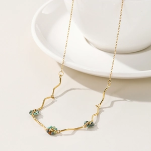 Handmade beaded flower necklace with gold wavy links and green stones on a white cup