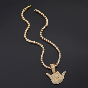 Macro view of iced-out gold Shaka gesture pendant on luxury tennis chain necklace