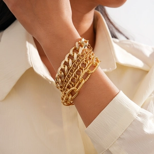 Detailed view of layered gold cuban and rope chain bracelets on a model's wrist