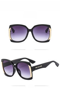 Detail view of square oversized sunglasses with black frame, gold trim and purple gradient lens