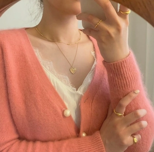 Close-up of a gold heart pendant necklace and rings styled with a pink knit cardigan