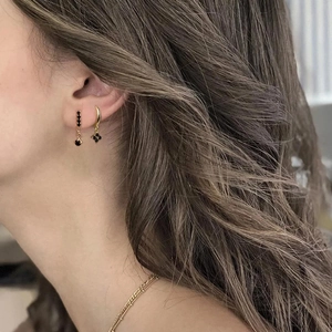 Close-up of gold ear hoops with black clover charms and layered necklaces on a model