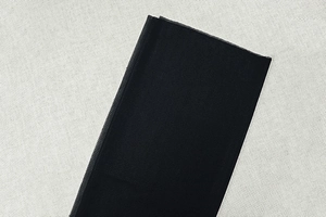 Detail shot of black pleated mesh fabric showing breathable texture on beige linen background