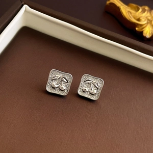 Macro shot of silver textured square stud earrings with embossed cherry pattern