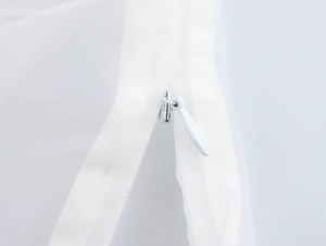 Detailed macro view of high-quality white invisible zipper on sheer organza fabric texture