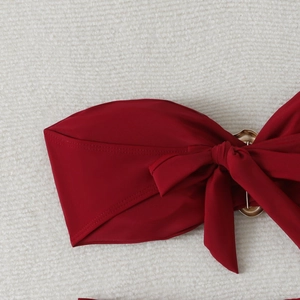 Detail of burgundy bikini top with a decorative bow and elegant gold metal ring link
