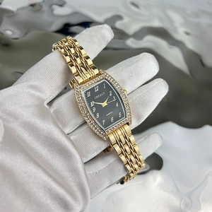 Macro view of gold tonneau watch with emerald rhinestones and black dial detailing