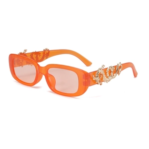 Detail of orange acetate sunglasses featuring gold dragon-shaped metal carvings on temples