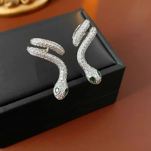Macro view of silver snake-shaped earrings with clear crystals and green gem eyes