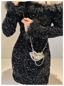 Silver lip-shaped clutch bag with metal chain shown with a sequined feather dress