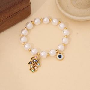 Detail of Hamsa hand and evil eye charms on a beaded pearl bracelet with gold accents