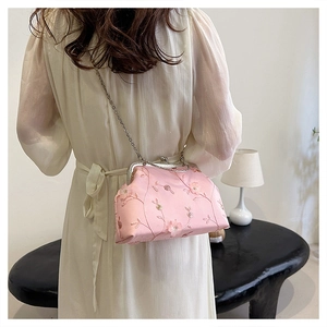 Pink embroidered clasp bag with floral detail and metal chain strap worn by a model