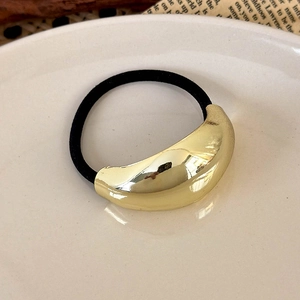 Close-up of golden geometric metal cuff on black elastic hair tie on white plate