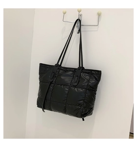 Close-up of a black quilted puffer tote bag hanging on a wall with glossy nylon texture