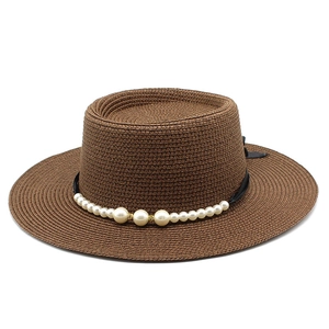 Dettaglio del cappello boater in paglia marrone con decorazione di perle e nastro nero