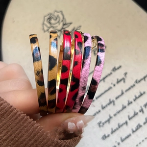 Detail of leopard print C-shape bangle bracelets in brown red and pink finishes
