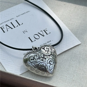 Vintage heart pendant necklace with intricate engravings on a simple black cord strap